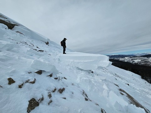 A person stands on a slab of snow on a potential avalanche slope.